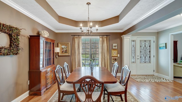 dining space with a chandelier, baseboards, a raised ceiling, and light wood-style floors