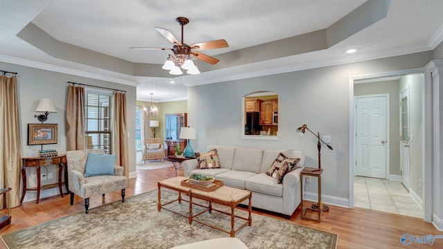 living area with light wood finished floors, a raised ceiling, a ceiling fan, and ornamental molding