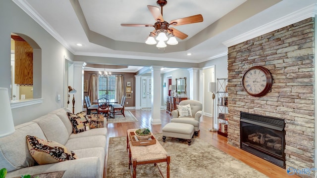 living area with crown molding, ceiling fan, decorative columns, wood finished floors, and a raised ceiling