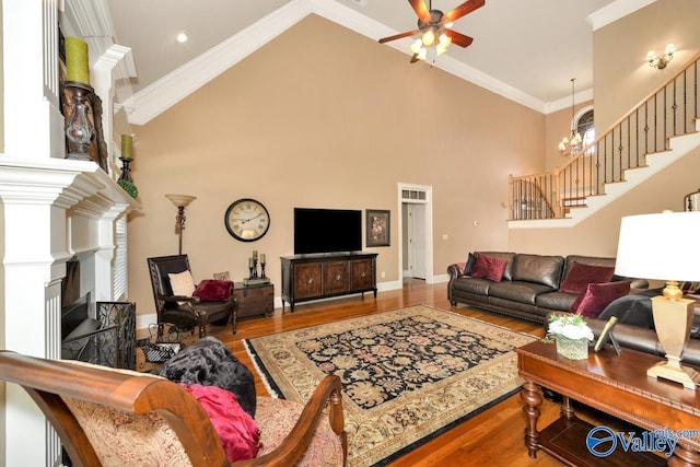 living room with hardwood / wood-style floors, crown molding, ceiling fan with notable chandelier, and a high ceiling