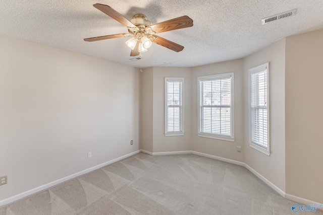 spare room with visible vents, light carpet, ceiling fan, a textured ceiling, and baseboards