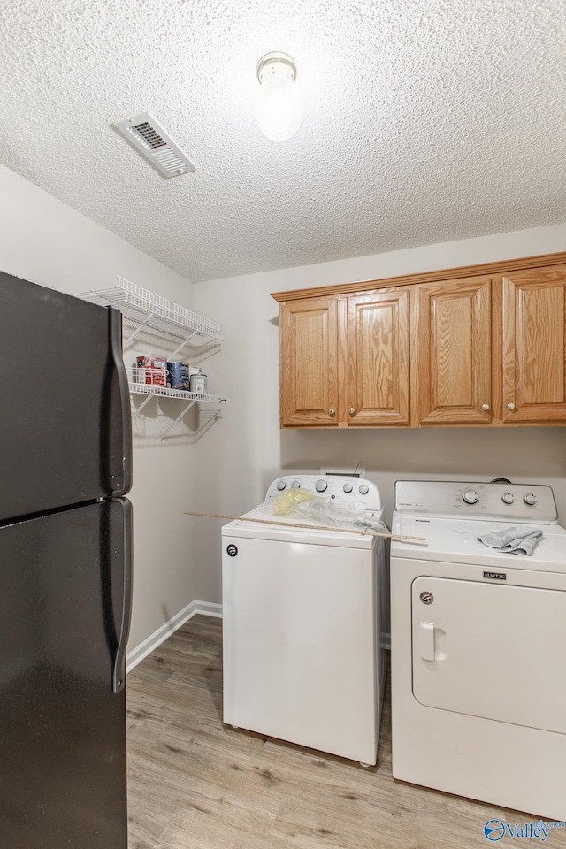 washroom with washing machine and dryer, visible vents, light wood-style flooring, and a textured ceiling