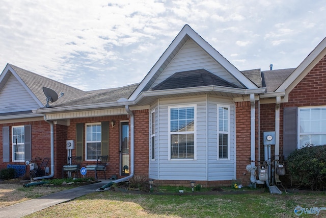 view of front facade featuring brick siding, a front lawn, and roof with shingles