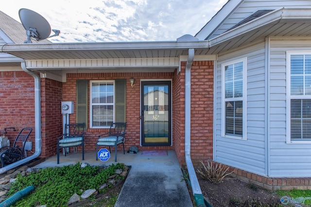 doorway to property with covered porch and brick siding