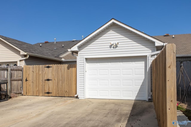 garage with concrete driveway, fence, and a gate