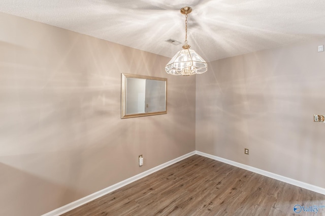 empty room with a chandelier, a textured ceiling, wood finished floors, visible vents, and baseboards