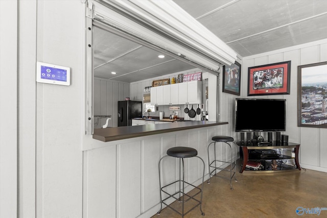 kitchen featuring concrete floors, a breakfast bar, black fridge, and white cabinets