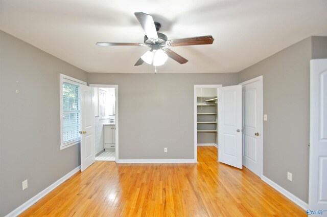 unfurnished bedroom featuring a closet, light hardwood / wood-style flooring, ensuite bath, a spacious closet, and ceiling fan