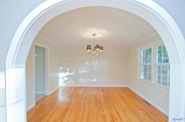 spare room featuring a chandelier, crown molding, and light wood-type flooring