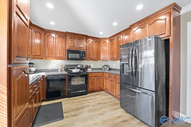 kitchen featuring brown cabinetry, dark countertops, light wood-style floors, and black appliances