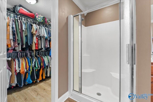 bathroom featuring a shower stall, a textured ceiling, a walk in closet, and wood finished floors