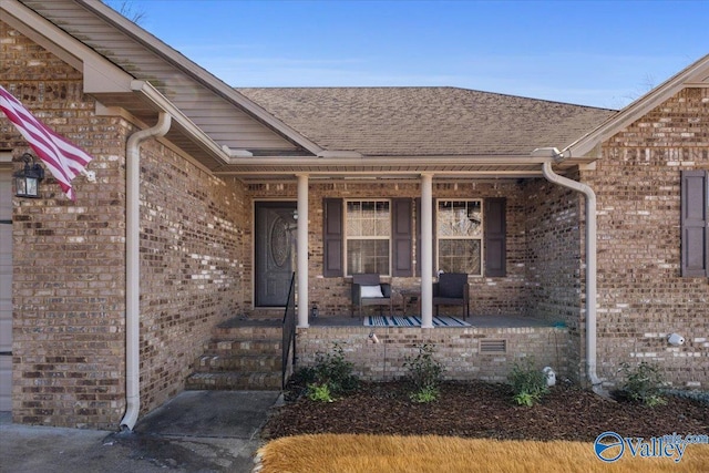 entrance to property featuring covered porch, brick siding, crawl space, and a shingled roof