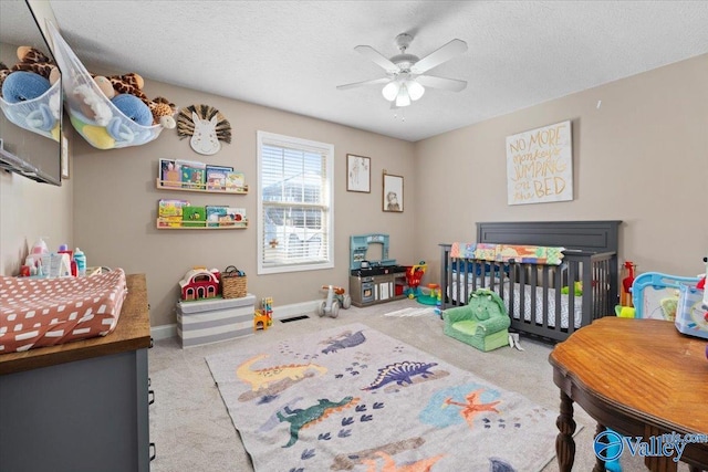 bedroom with a nursery area, light colored carpet, a textured ceiling, and baseboards