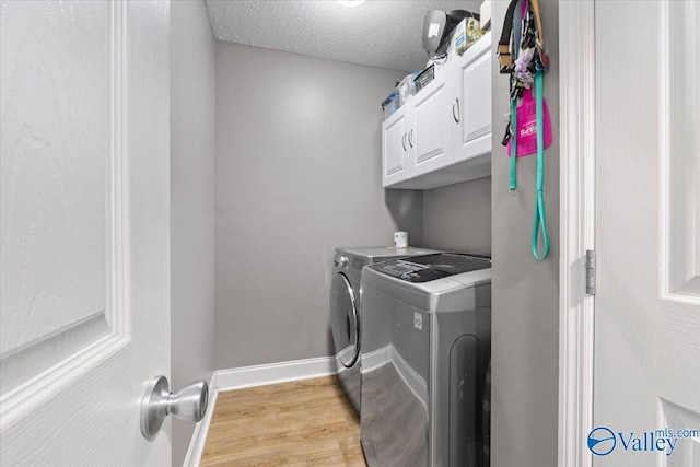 clothes washing area with cabinet space, baseboards, light wood-style flooring, independent washer and dryer, and a textured ceiling