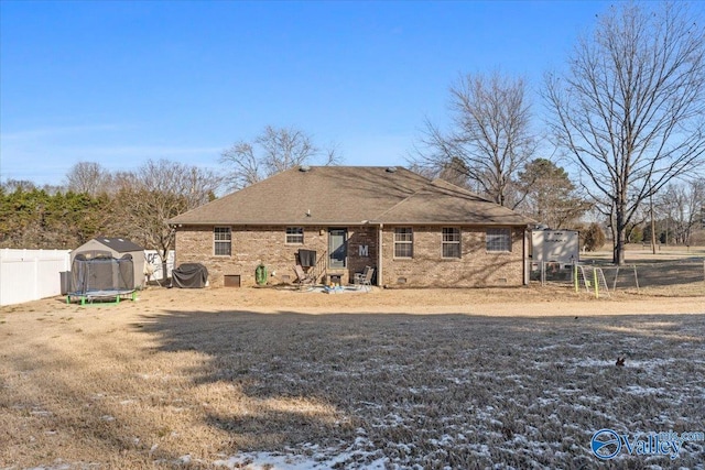 rear view of house with crawl space, a trampoline, fence, and brick siding