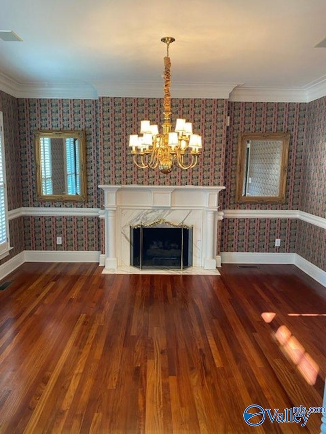 unfurnished living room featuring a premium fireplace, crown molding, wood-type flooring, and a notable chandelier