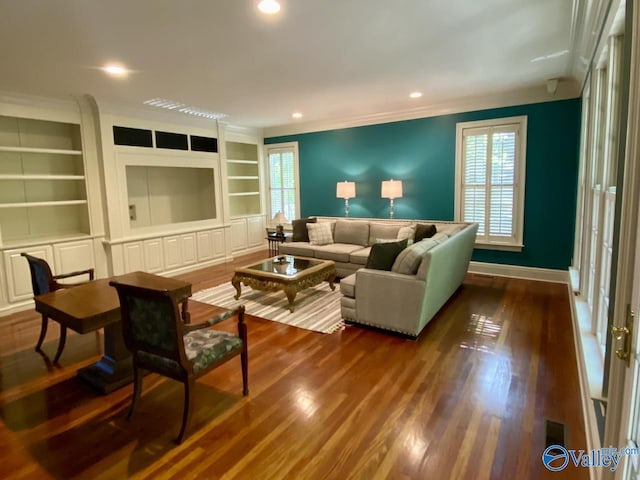 living room featuring dark wood-type flooring, ornamental molding, built in features, and a wealth of natural light