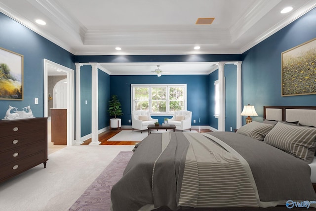 bedroom with crown molding, a tray ceiling, light wood-type flooring, and ornate columns