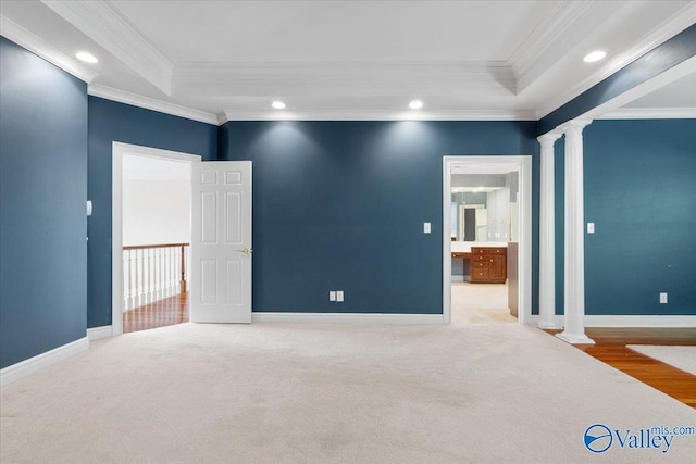 empty room with crown molding, a raised ceiling, and ornate columns