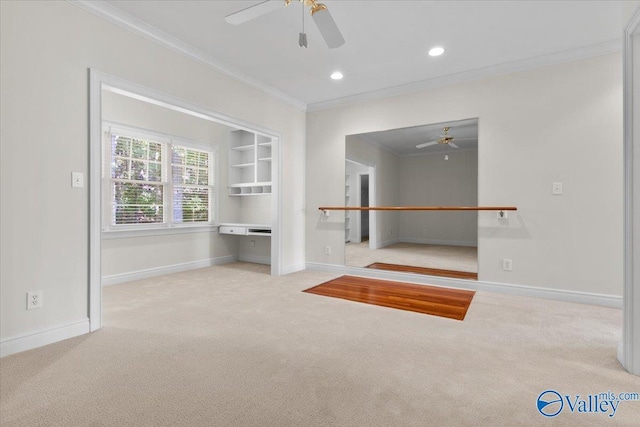 interior space with crown molding, ceiling fan, built in desk, and light carpet