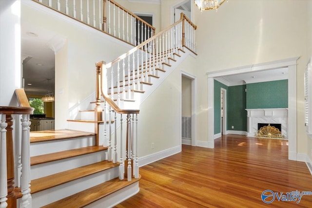 stairs with a high ceiling, crown molding, hardwood / wood-style floors, and a high end fireplace