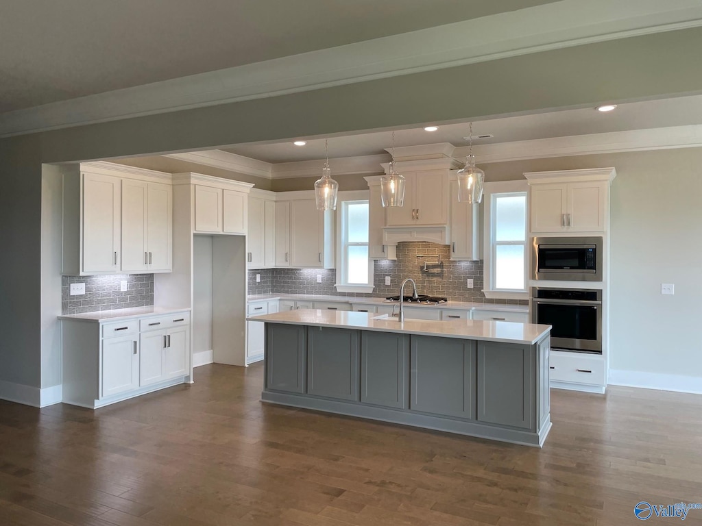 kitchen with white cabinetry, dark hardwood / wood-style flooring, decorative light fixtures, a kitchen island with sink, and appliances with stainless steel finishes