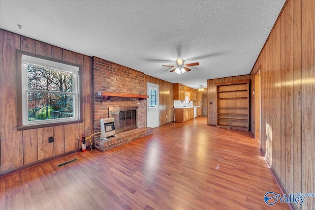 unfurnished living room featuring visible vents, light wood-style floors, wood walls, and a textured ceiling