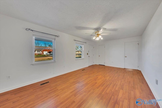 unfurnished room featuring visible vents, a textured ceiling, light wood-type flooring, and baseboards