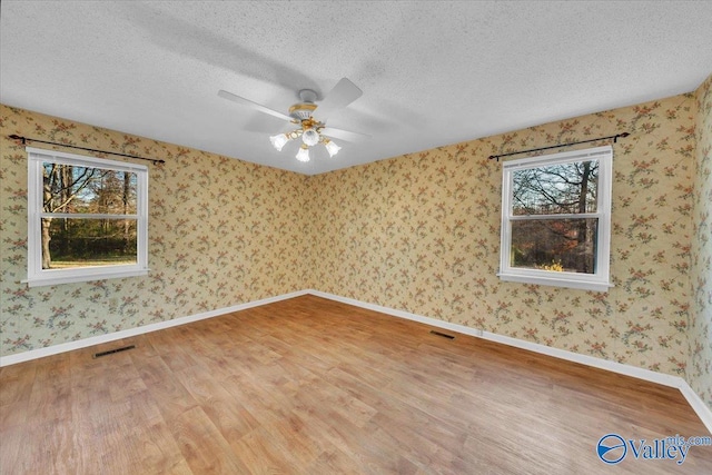 spare room featuring visible vents, a textured ceiling, wood finished floors, wallpapered walls, and baseboards