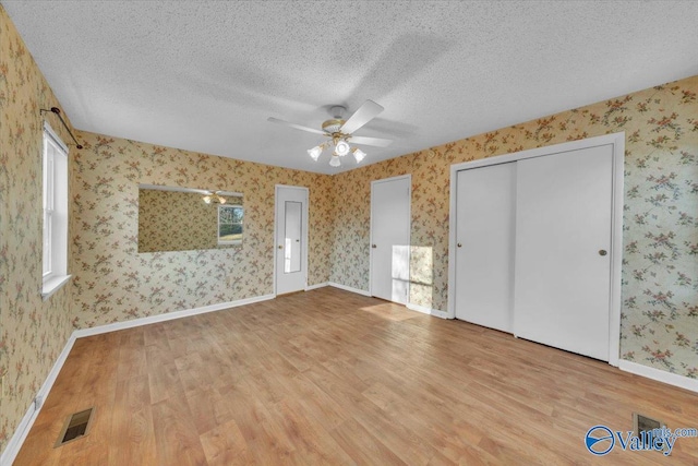 unfurnished bedroom with wood finished floors, baseboards, visible vents, wallpapered walls, and a textured ceiling