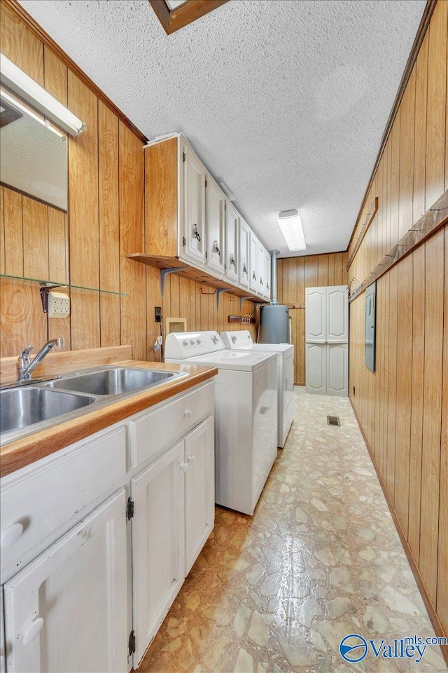 washroom featuring separate washer and dryer, cabinet space, a sink, wood walls, and a textured ceiling