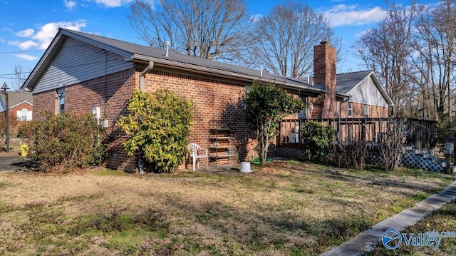 view of home's exterior with a wooden deck, brick siding, a chimney, and a lawn