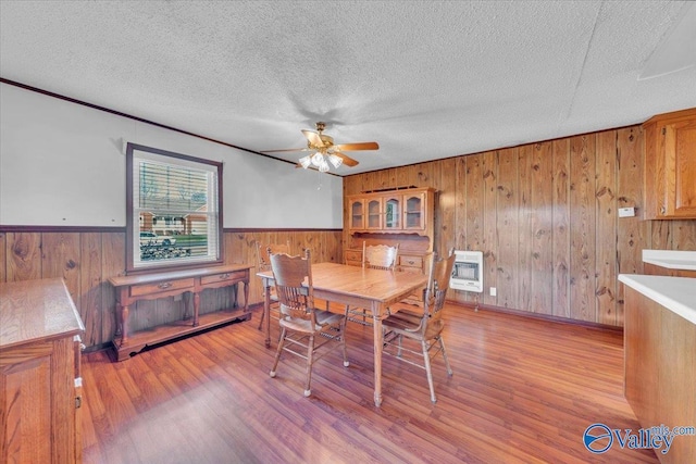 dining area with a textured ceiling, heating unit, wood finished floors, and wainscoting