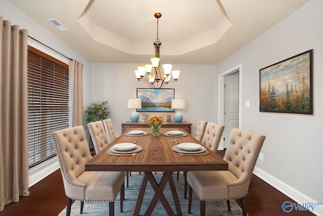 dining area featuring dark wood-type flooring, a tray ceiling, and a chandelier