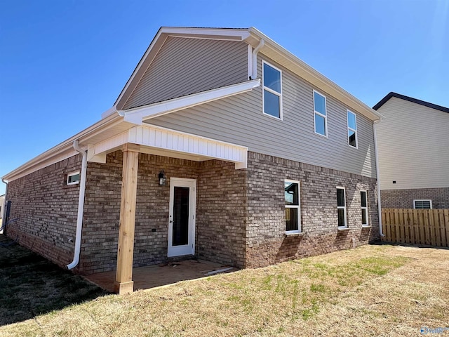 back of property with a patio, brick siding, a lawn, and fence