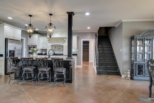 kitchen featuring white cabinetry, hanging light fixtures, appliances with stainless steel finishes, stone counters, and a kitchen island with sink