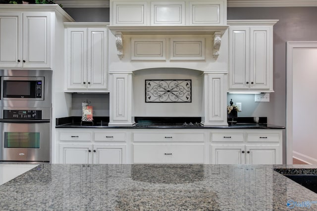 kitchen featuring white cabinetry, ornamental molding, stainless steel appliances, and dark stone counters