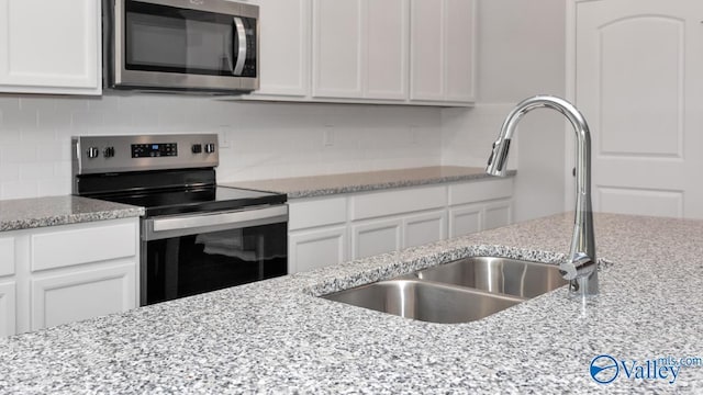 kitchen with light stone counters, sink, white cabinets, and stainless steel appliances