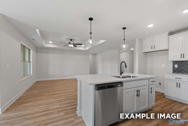 kitchen featuring stainless steel dishwasher, a tray ceiling, a sink, and light wood-style flooring