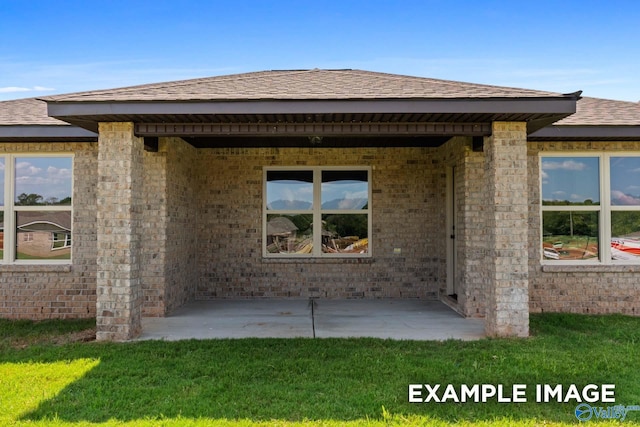 rear view of house featuring a lawn, brick siding, a patio area, and roof with shingles