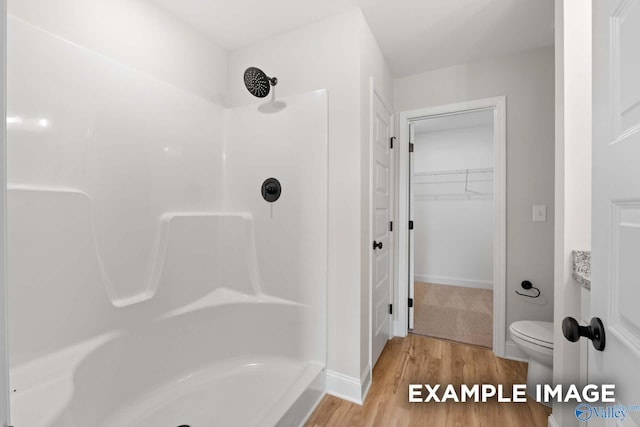 full bath featuring wood finished floors, a spacious closet, a shower, and toilet