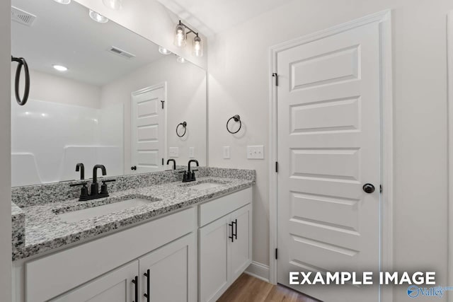 bathroom with wood finished floors, visible vents, a sink, and double vanity