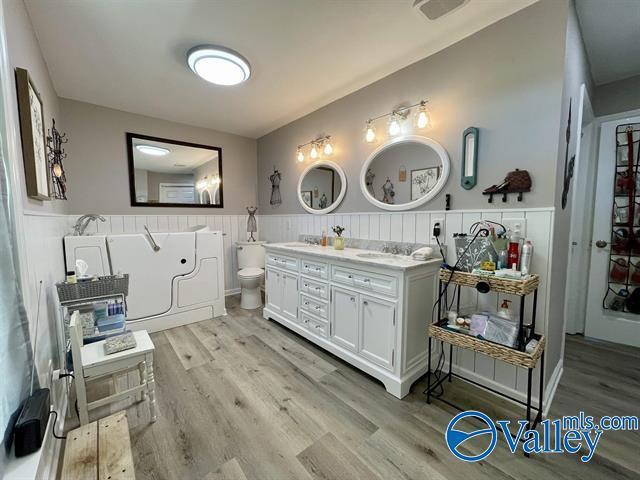 bathroom featuring a sink, double vanity, a wainscoted wall, and wood finished floors