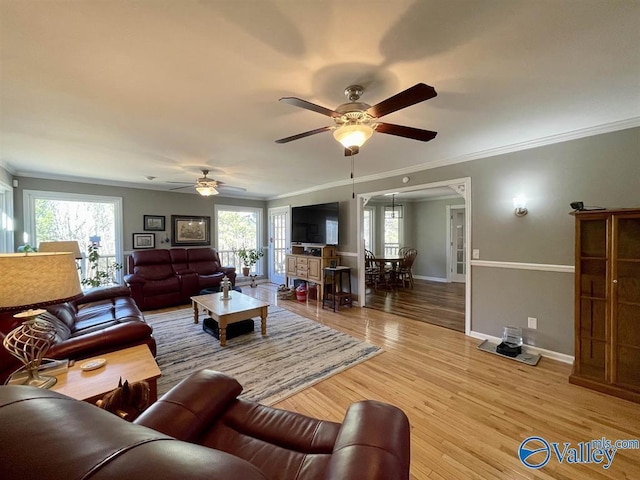 living area with crown molding, ceiling fan, baseboards, and a wealth of natural light