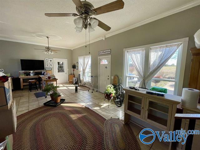 living area featuring crown molding, light tile patterned floors, a ceiling fan, and a textured ceiling