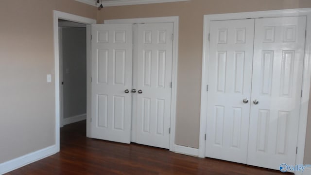 unfurnished bedroom featuring multiple closets, crown molding, and dark wood-type flooring