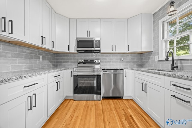 10012 Allison Dr, Huntsville, AL 35803 - kitchen with stainless steel appliances, a sink, light wood-style floors, white cabinets, and decorative backsplash