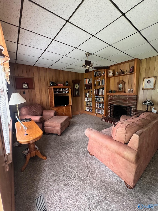 carpeted living room with a brick fireplace, wooden walls, and a paneled ceiling