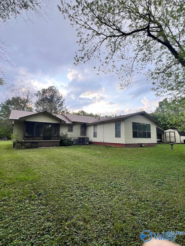 back of property with a sunroom, a yard, and a storage shed