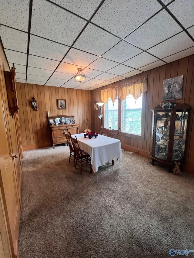 dining room with wood walls, light carpet, and a paneled ceiling